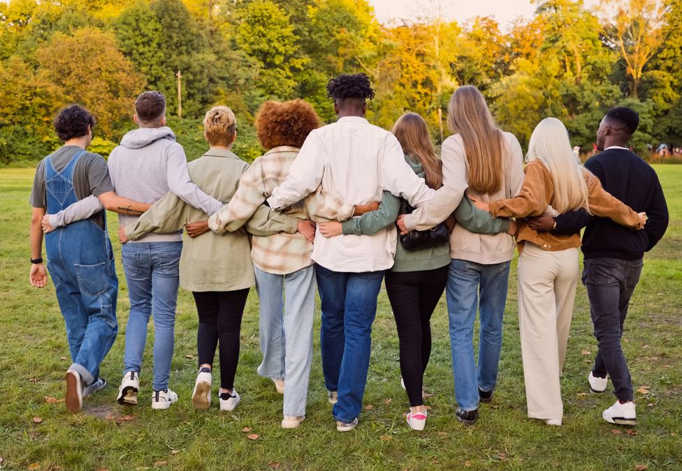 An image of a group of people, facing their backs. They are a diverse group of adult people walking with their arms around each other through a field, leading to an article from the Milken Institute titled "How Philanthropy Can Support a Community-Centered Biomedical Research Ecosystem to Achieve Health Equity".