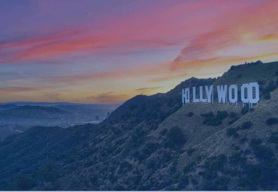 An image of the HOLLYWOOD sign of Los Angeles, located in mountainous terrain with a colorful sunset in the background and a dark overlay on the image.