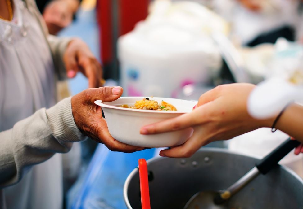 An image of someone's hands, handing over a bowl of food to another person's hands.