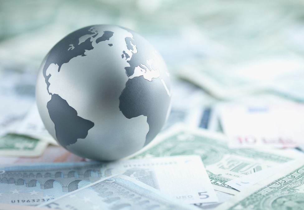 An image of a grayscale globe of Earth sitting upon various paper currencies.