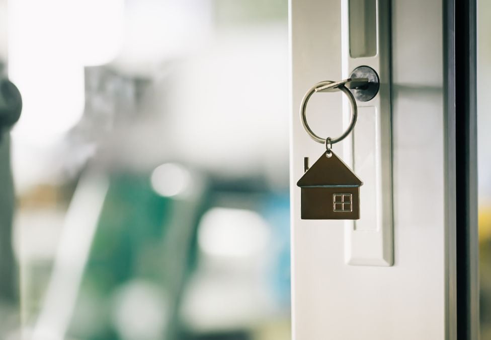 An up close image of a key inside of the lock of a white door with a hanging keychain that is shaped like a house.