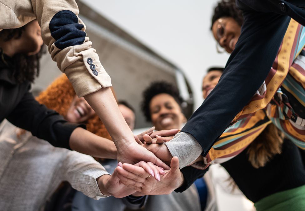 An image of a diverse group of people all putting their hands together in a circle.