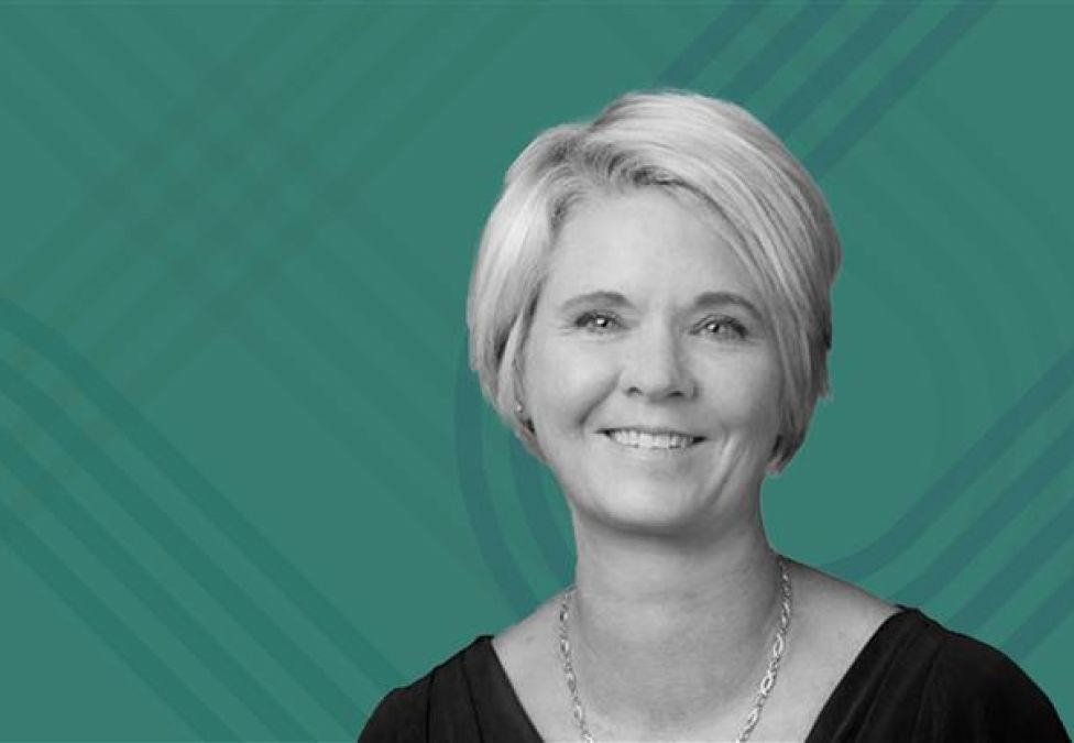 Black-and-white photo of Ginger Gregory, Chief Human Resources Officer at Biogen, smiling against a teal background with abstract line patterns. 
