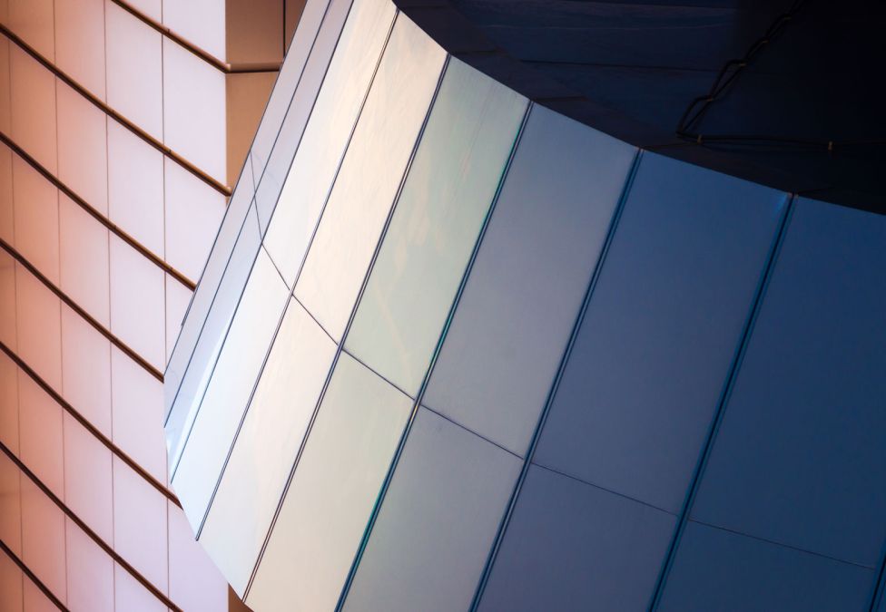 Close-up of a modern building with reflective angled panels in shades of blue and beige.