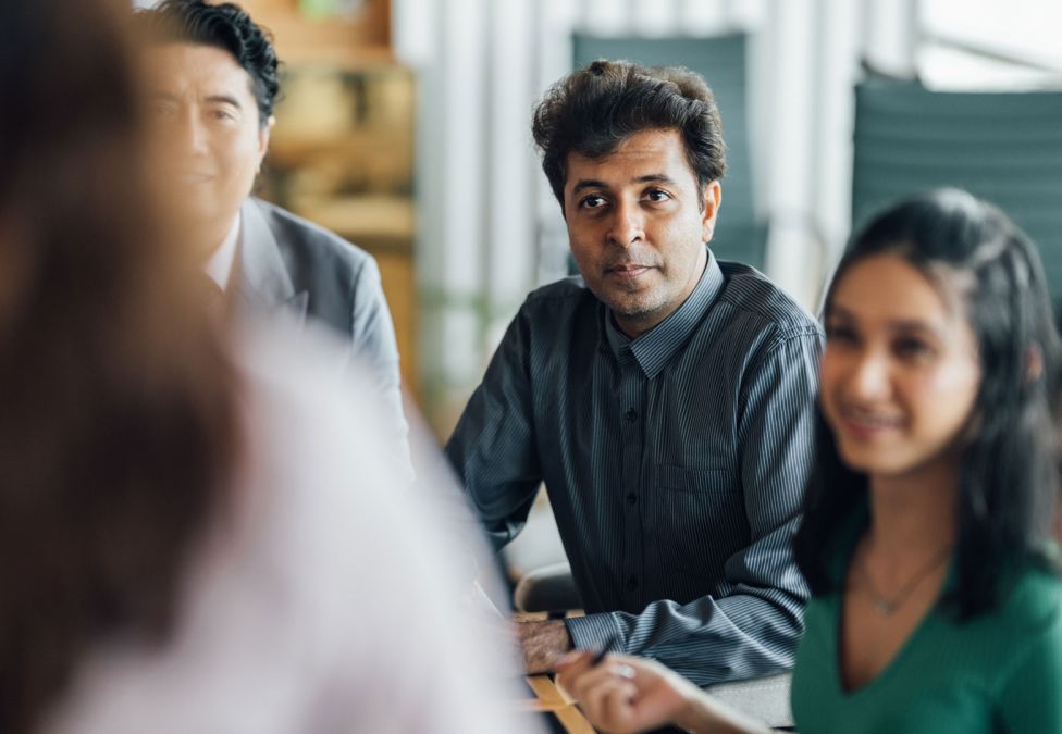 Group of professionals sitting around a conference table, listening attentively in a collaborative meeting.
