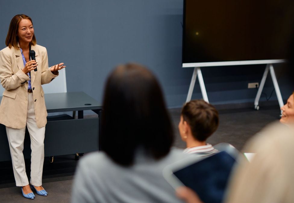 Professional woman holding a microphone while speaking to an audience in a business setting.