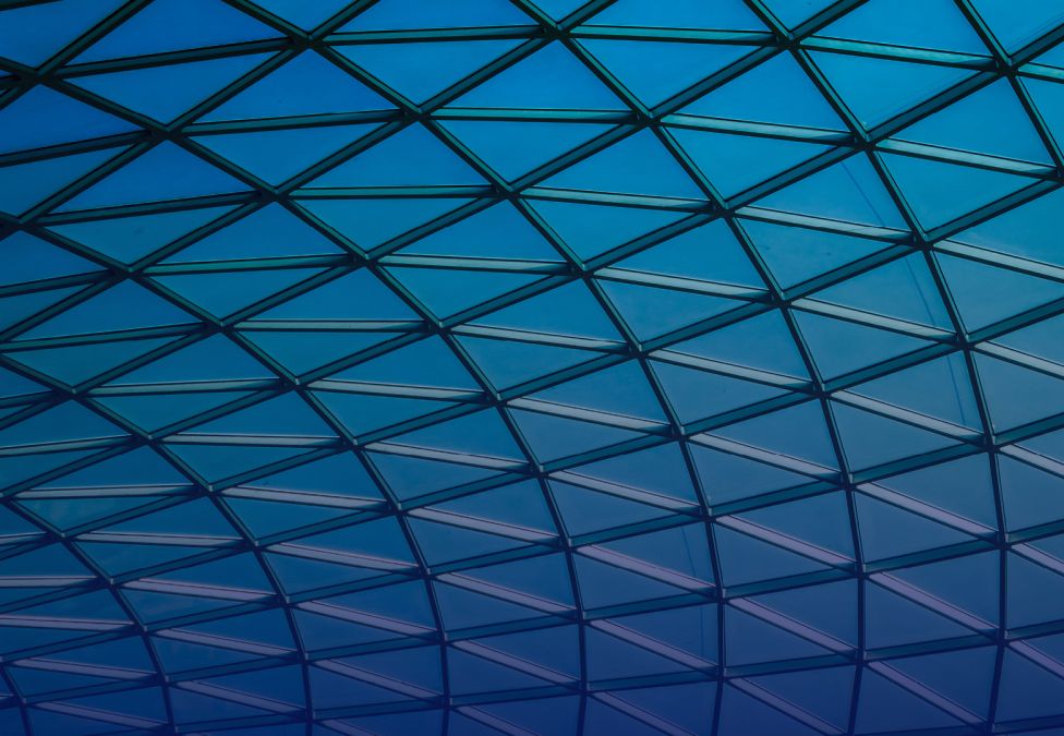 Geometric glass roof with triangular grid pattern in blue gradient light.