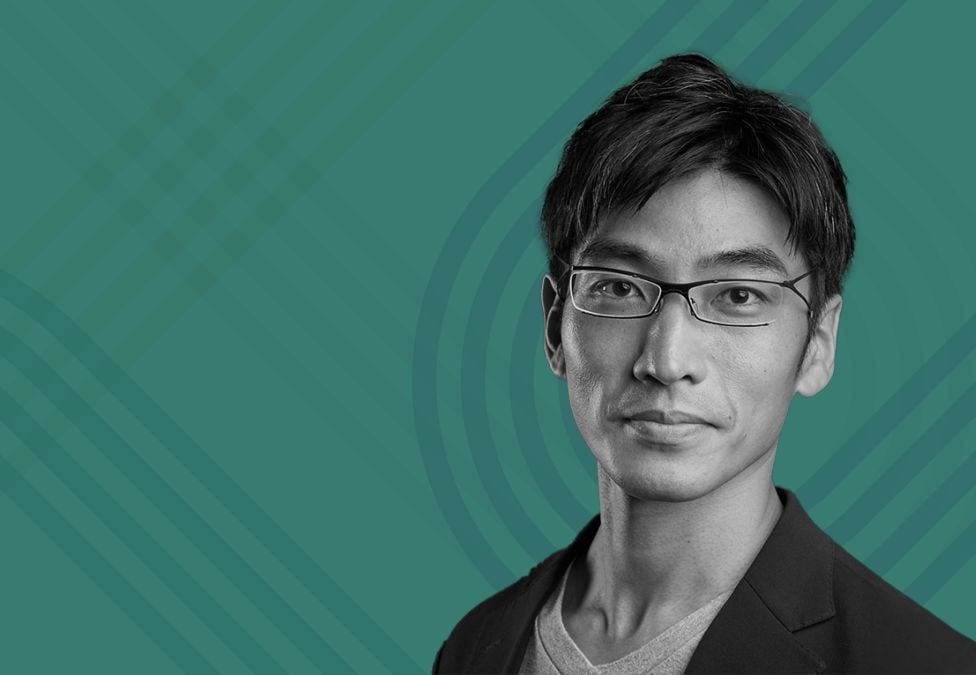 Portrait of a man with short dark hair and glasses, wearing a blazer over a T-shirt, on a teal background with the Milken Institute logo in the top left corner.