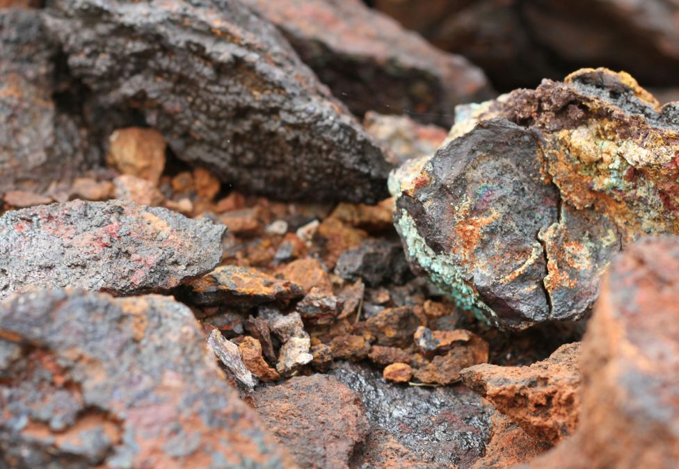 Close-up view of raw mineral rocks with rough, textured surfaces in shades of brown, orange, gray, and green.