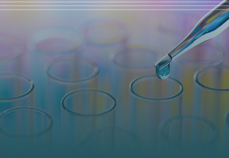 A close-up of a pipette releasing a drop of liquid into a row of transparent test tubes, with a soft blue and purple gradient background suggesting a laboratory or scientific research setting.