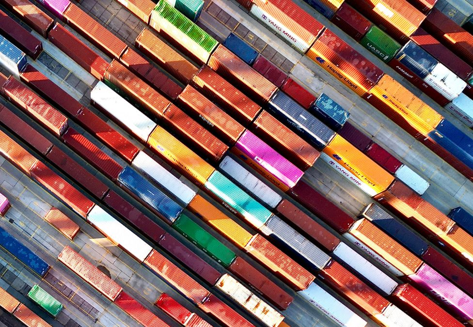 Aerial view of colorful shipping containers neatly arranged in rows at a port or storage yard.