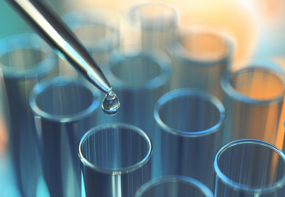 Pipette dispensing a liquid droplet into a row of laboratory test tubes.