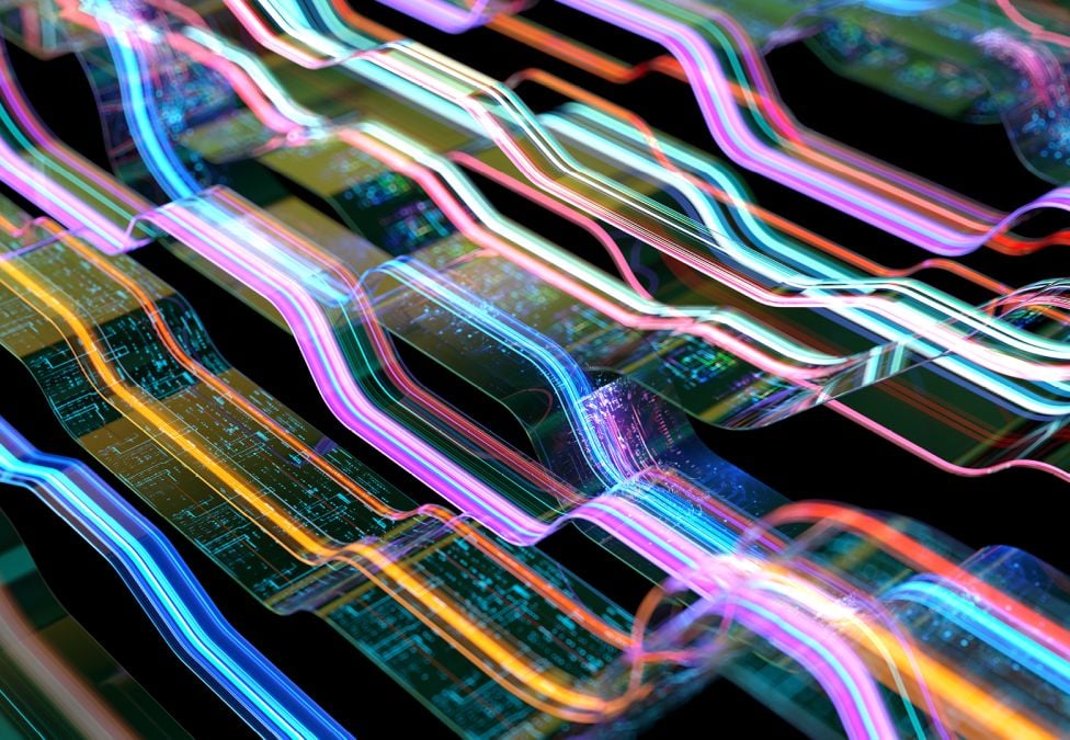Abstract 3D digital illustration of glowing, multicolored wave streams flowing over layered circuit board surfaces against a black background, evoking data transmission or AI processing.