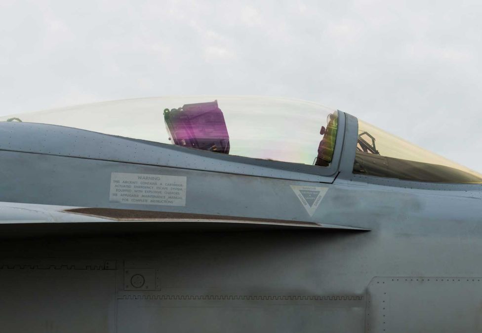 Close-up side profile of a grey fighter jet’s cockpit canopy against a cloudy sky.