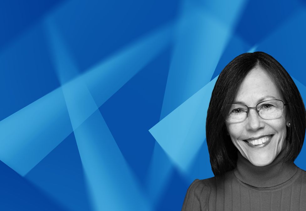 Headshot of a smiling woman with dark shoulder-length hair and glasses, set against a blue geometric background.