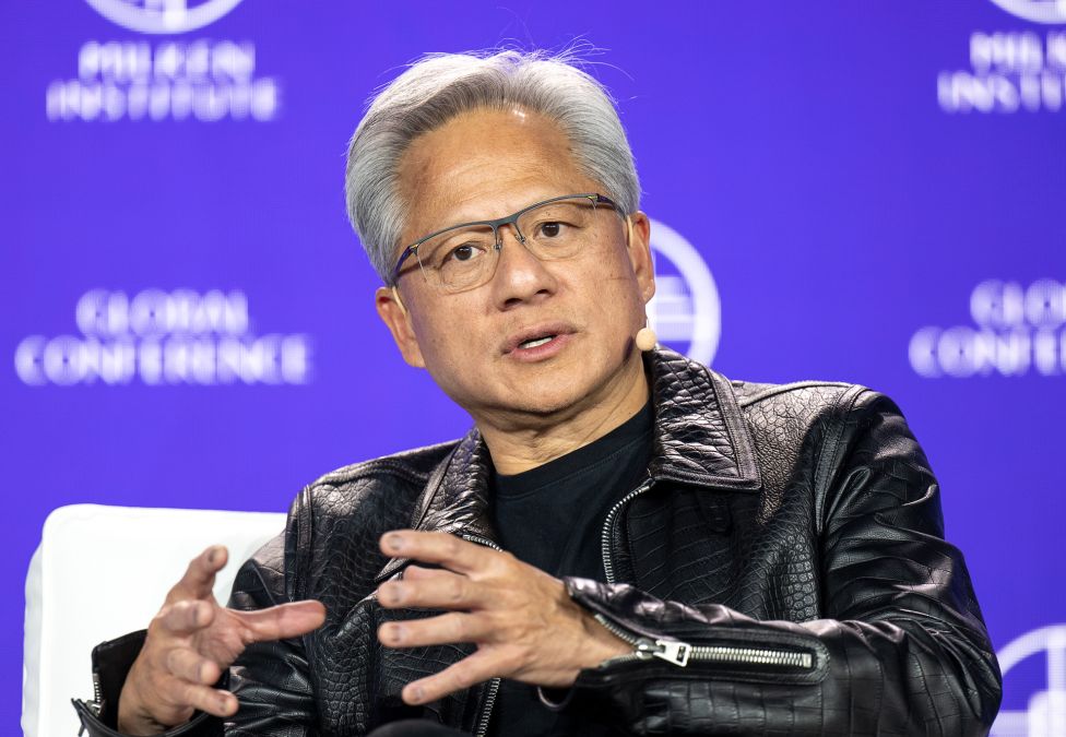 Man in glasses and black leather jacket speaking at conference with blue backdrop
