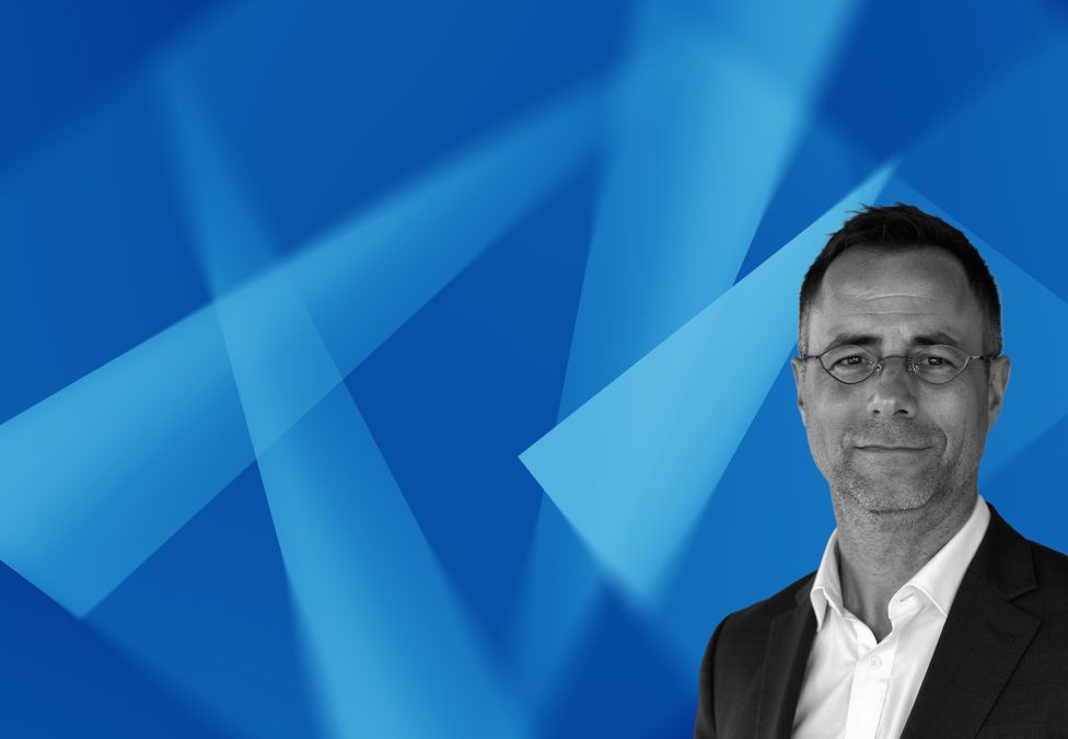 Professional headshot of businessman in suit against blue geometric background