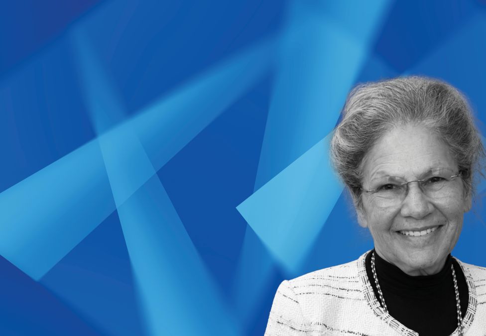 Professional woman in white blazer smiling against blue geometric background