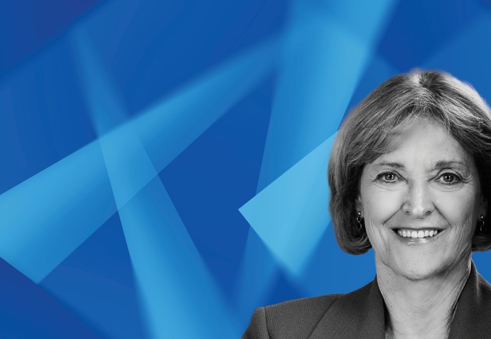 Professional headshot of smiling woman against blue geometric background