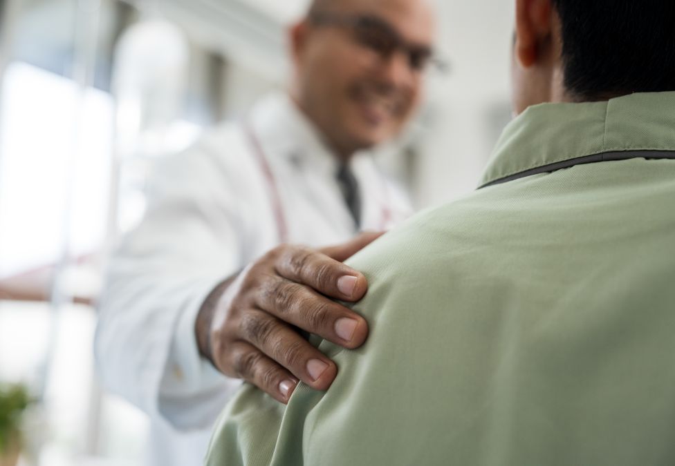 Doctor in white coat with hand on patient's shoulder