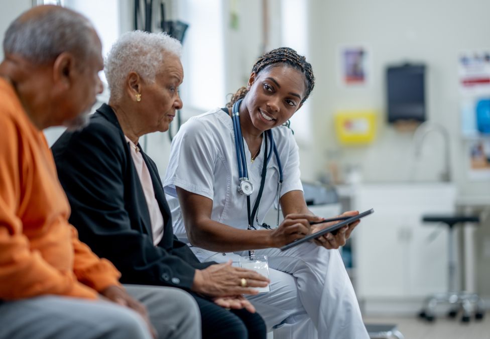 Healthcare worker showing tablet to two elderly patients in medical waiting room