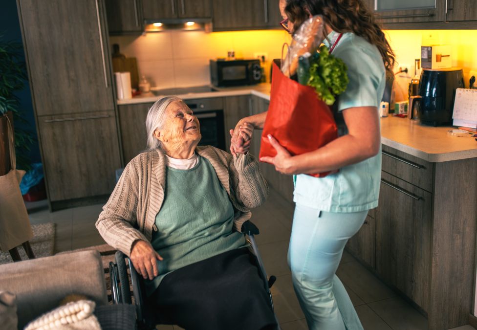 Woman presenting flowers to elderly woman seated in kitchenette 