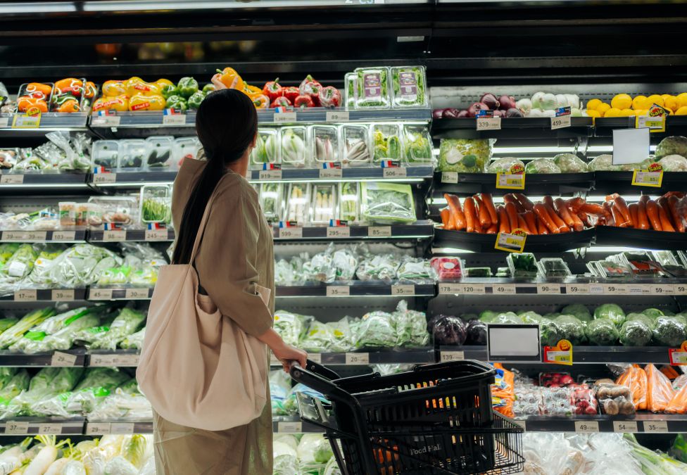 Woman with shopping basket browsing fresh produce aisle in grocery store