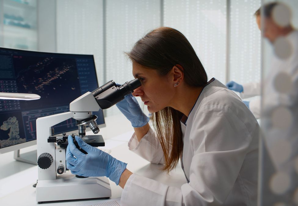 Scientist in white lab coat looking through microscope in laboratory