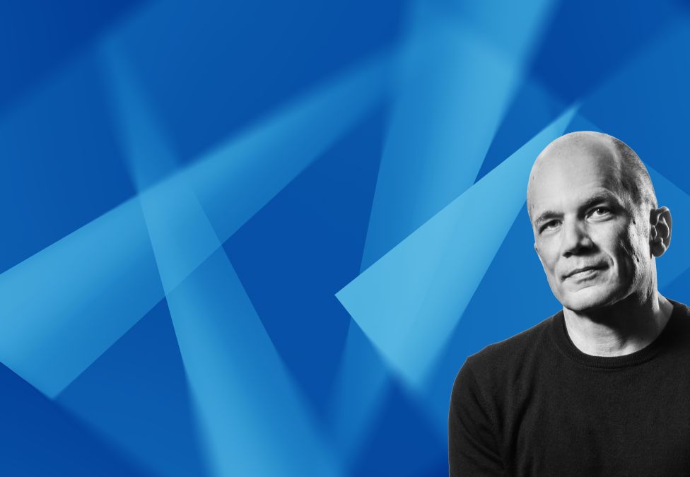 Man in black shirt smiling against blue geometric background