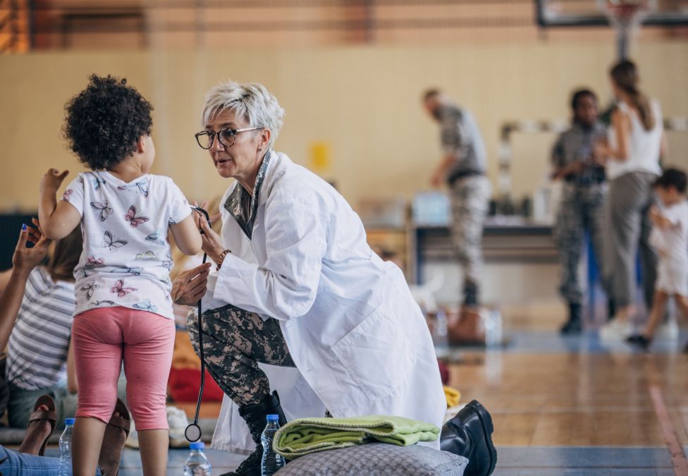Healthcare worker in white coat kneeling while assisting a young child