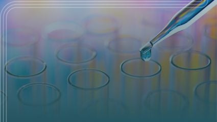 A close-up of a pipette releasing a drop of liquid into a row of transparent test tubes, with a soft blue and purple gradient background suggesting a laboratory or scientific research setting.